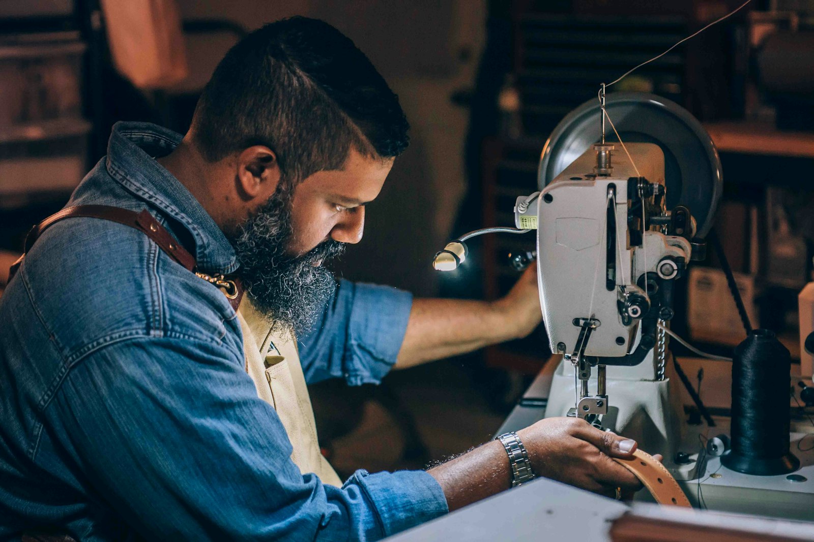 A tailor bent over a sewing machine in the atelier